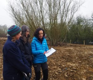 Three women standing in a muddy field looking at a clipboard